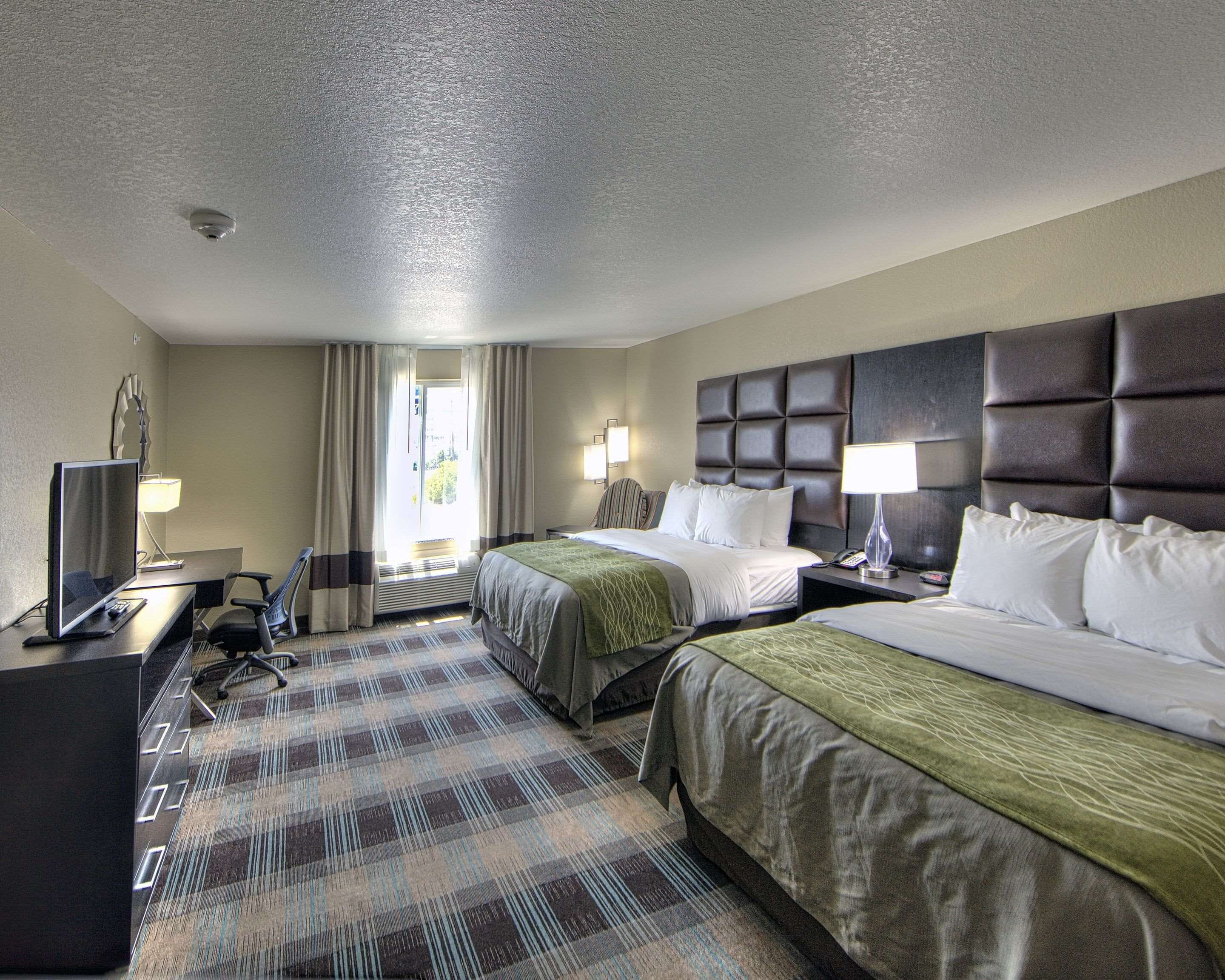 A hotel room with two beds, a desk with a computer, a chair, a TV, and a window with curtains.