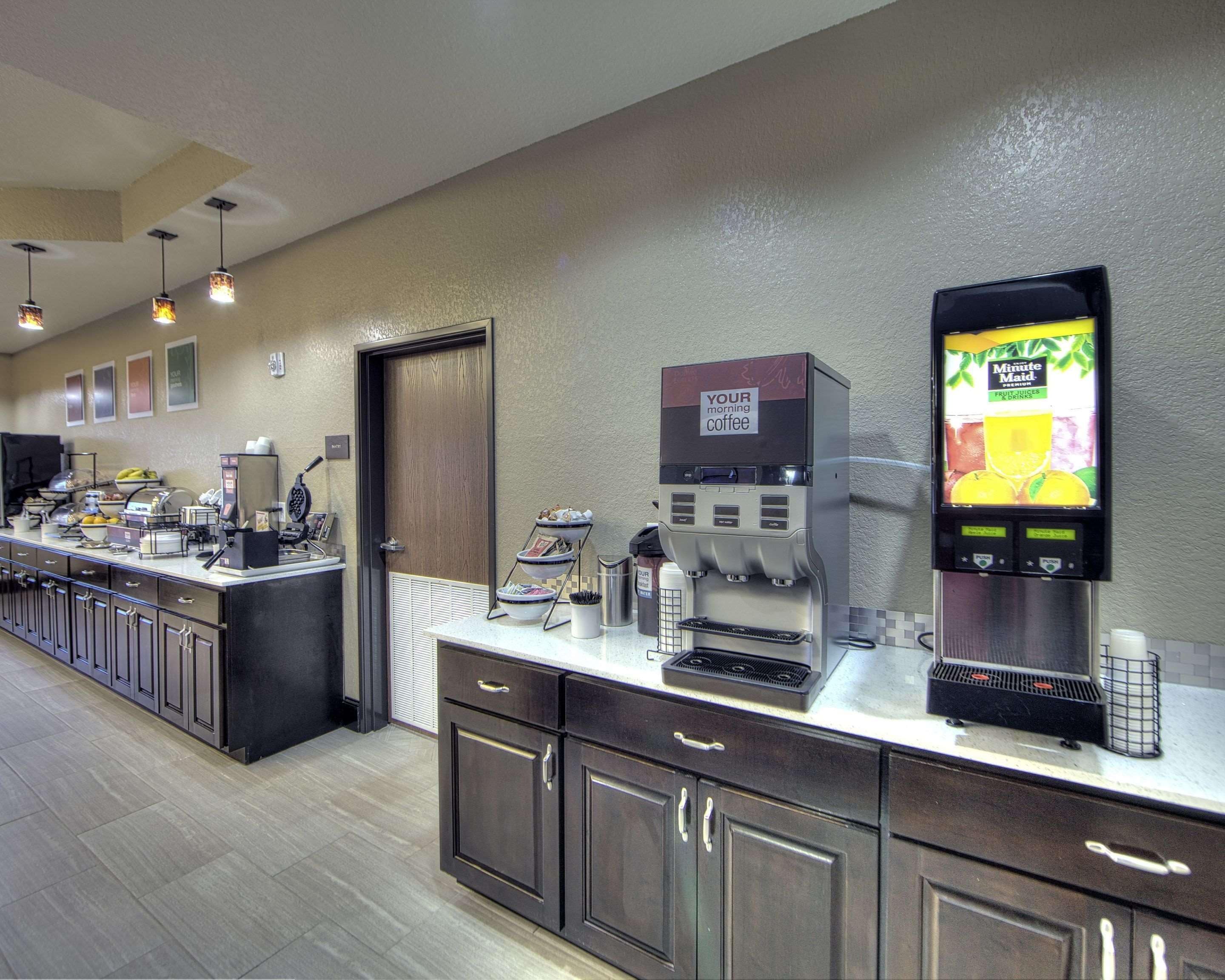A breakfast bar with coffee machines, a waffle maker, and a fruit juice dispenser.