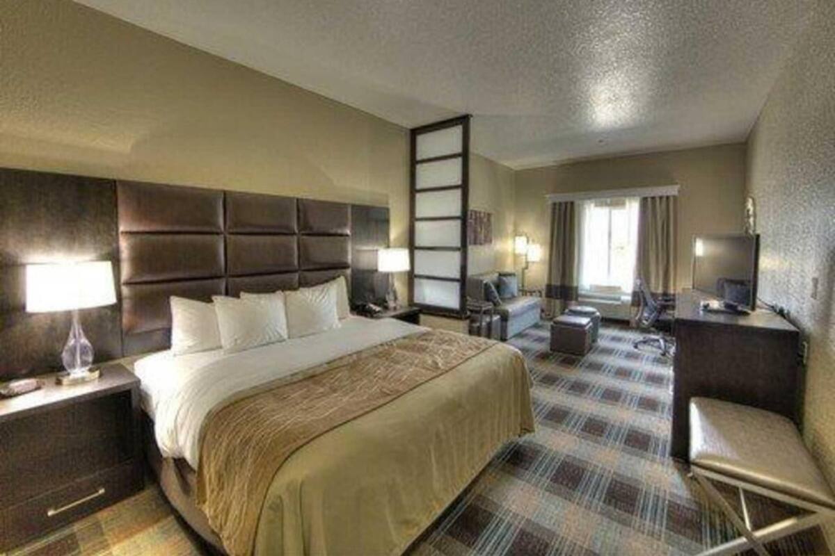 A hotel room with a large bed, a desk, a chair, a TV, and a window with curtains.