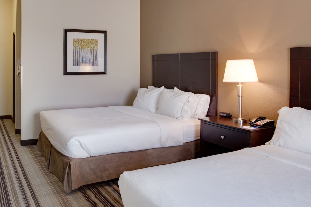 A hotel room with two beds, a nightstand with a lamp, a framed picture on the wall, and a carpeted floor.