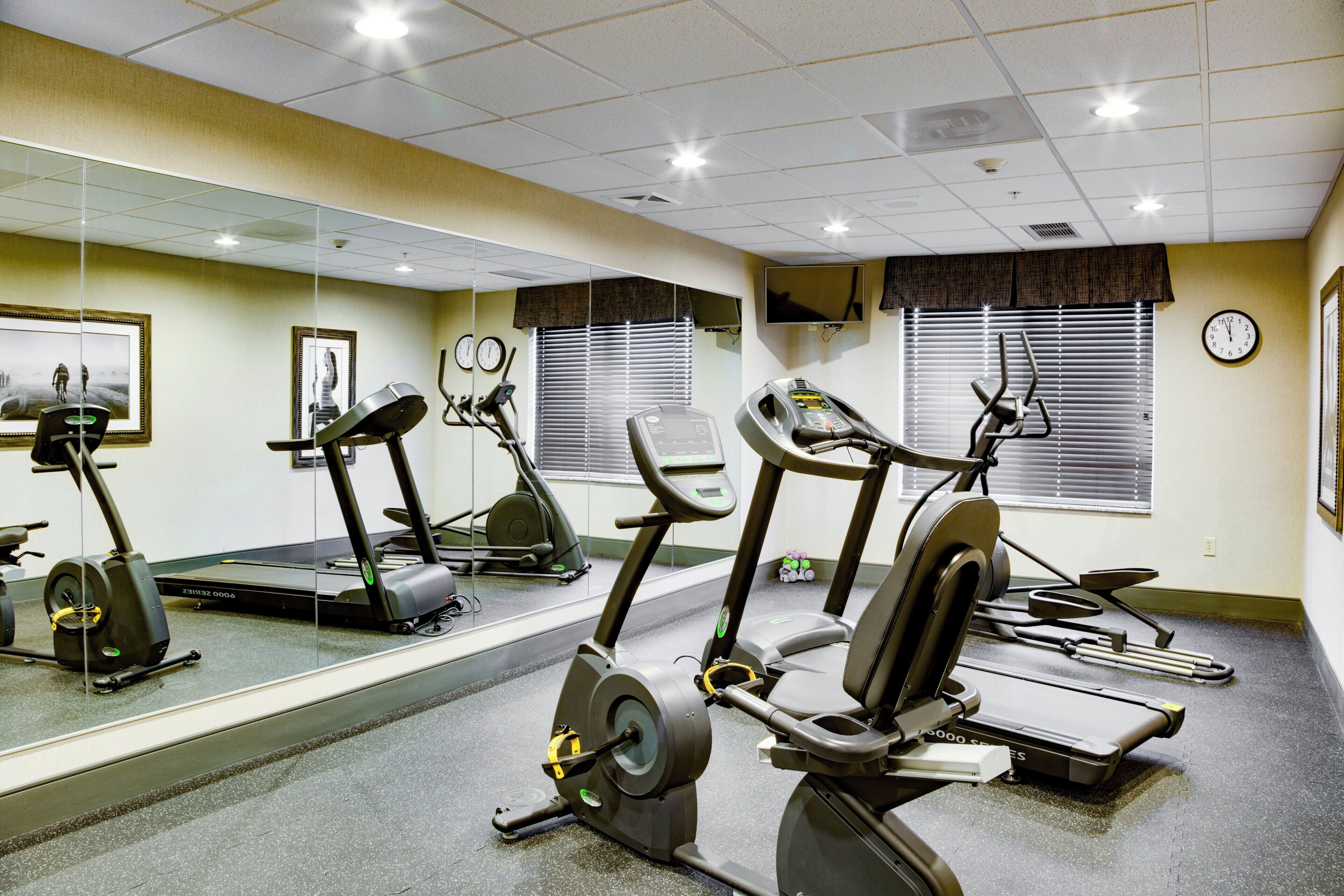 Un gimnasio con bicicletas estáticas, cintas de correr y un espejo grande.