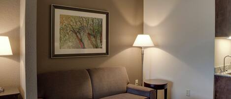 A hotel room with a sofa, a table, a lamp, and a painting on the wall.