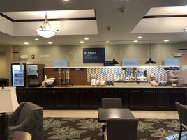 Un área de desayuno de hotel con un mostrador de autoservicio, asientos y un letrero que anuncia que el desayuno está listo.