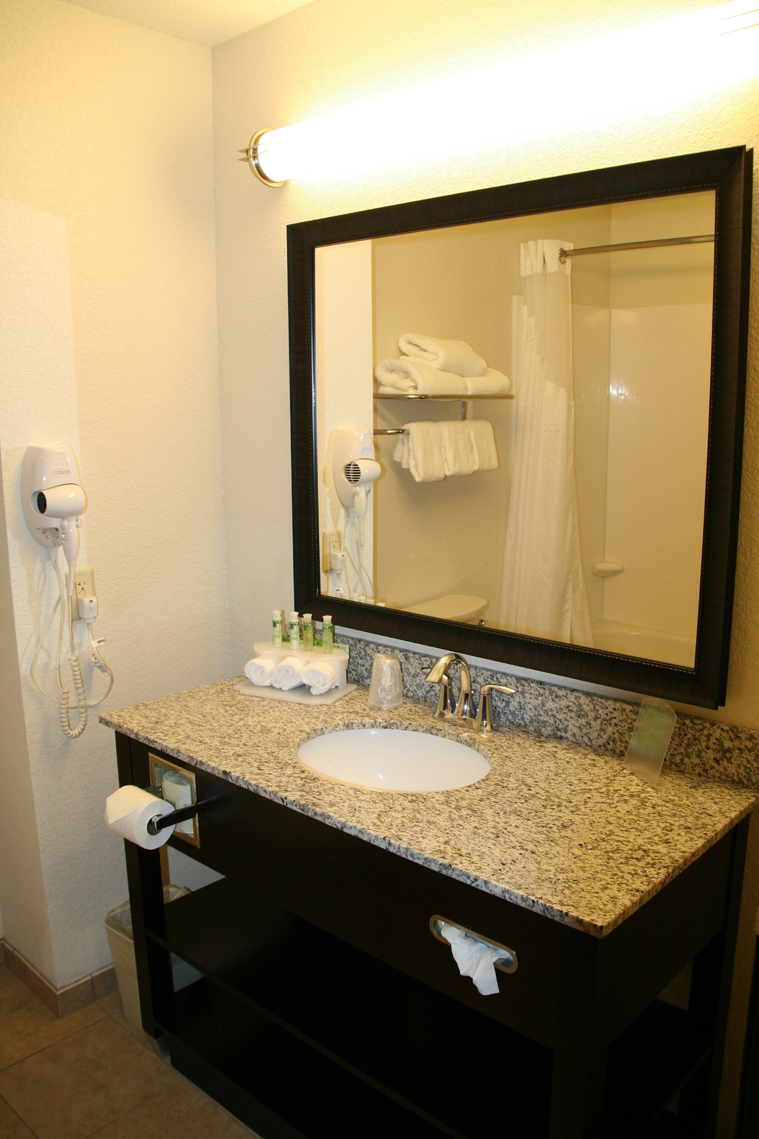 Casa de banho com lavatório, espelho, porta-toalhas e secador de cabelo.