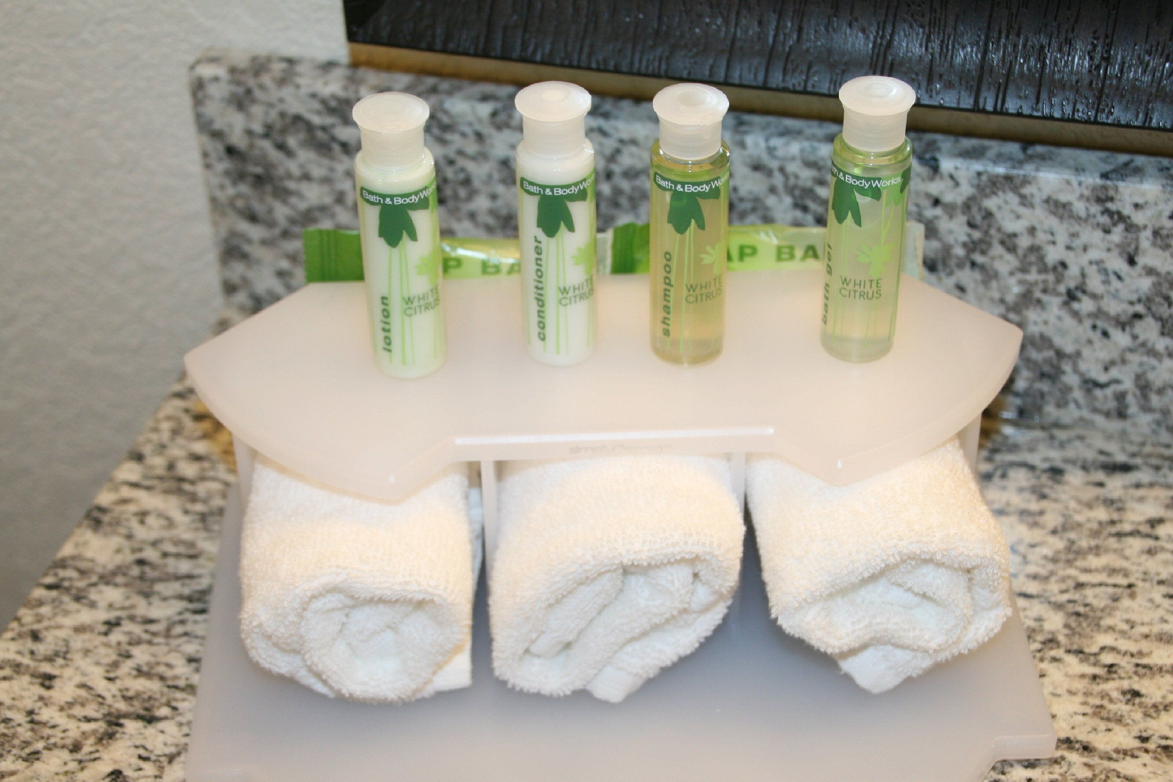 Tocador de baño con un toallero blanco que sostiene tres toallas y cuatro botellas de gel de ducha cítrico blanco.