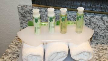 Tocador de baño con un toallero blanco que sostiene tres toallas y cuatro botellas de gel de ducha cítrico blanco.
