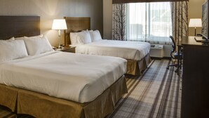 Une chambre d’hôtel avec deux lits, un bureau, une chaise, une lampe et une fenêtre avec des rideaux.