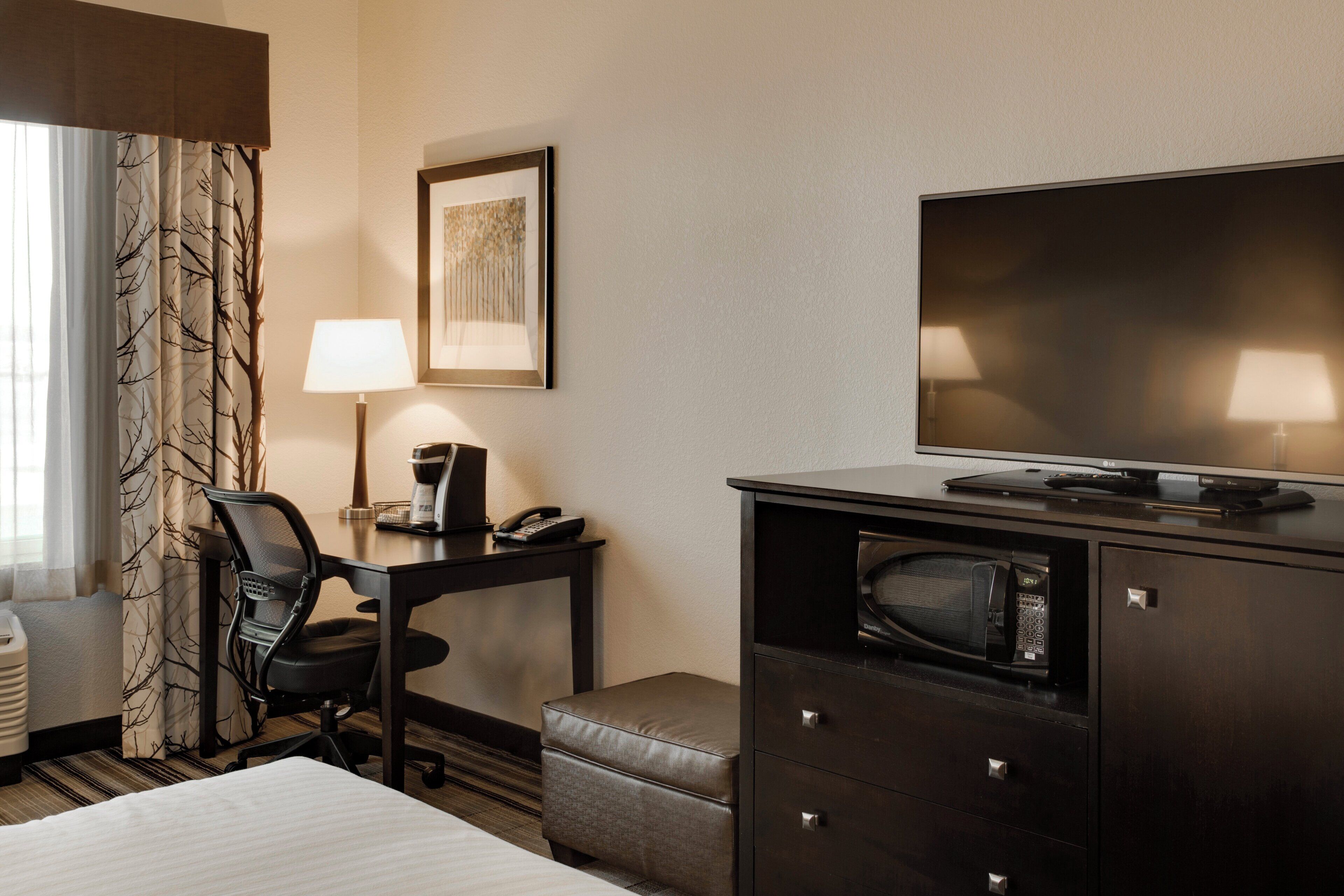 A hotel room with a bed, a desk with a telephone and lamp, a television, a microwave, and a chair.