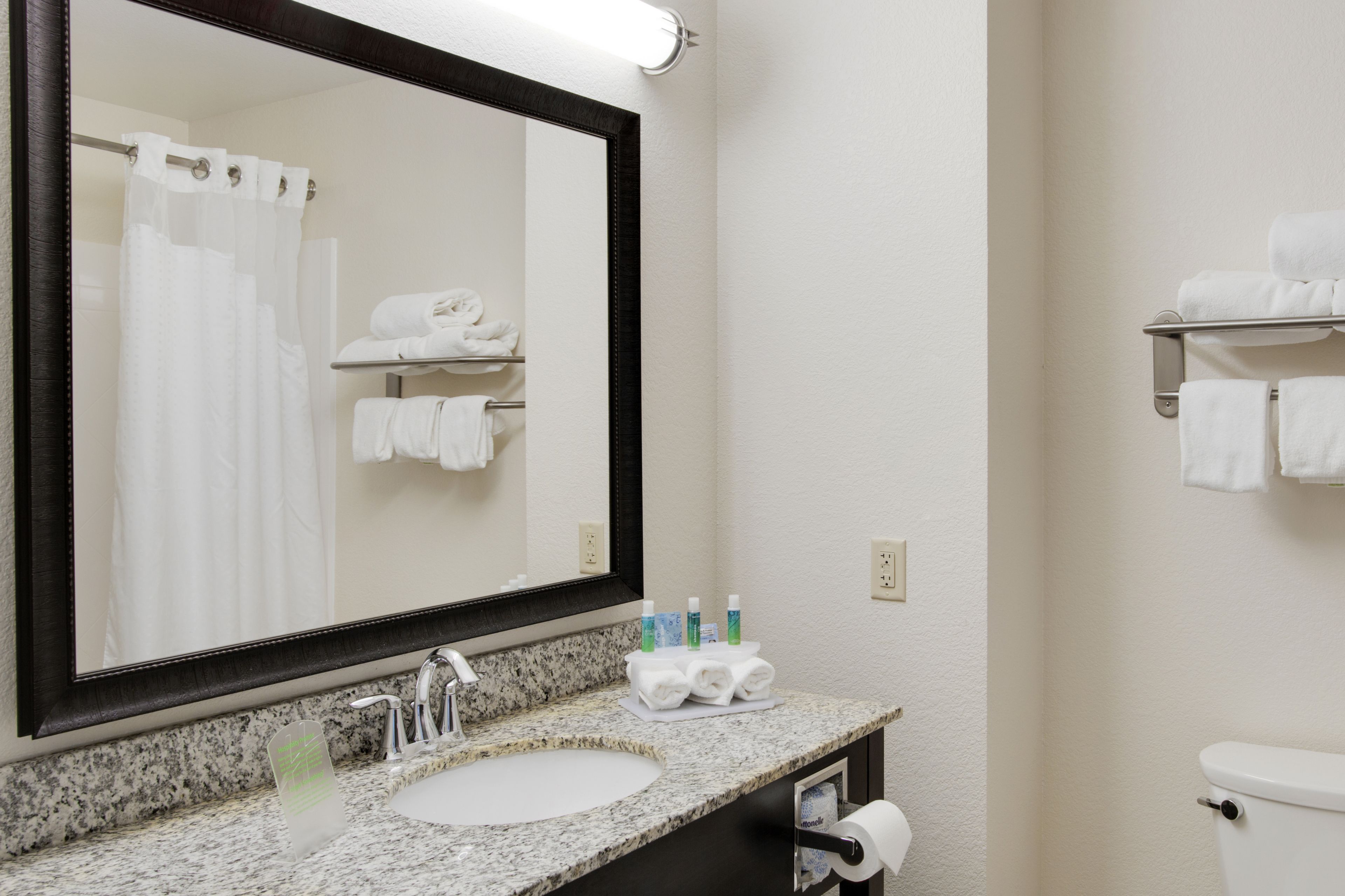 A bathroom with a large mirror, a sink, a toilet, and a towel rack with towels.