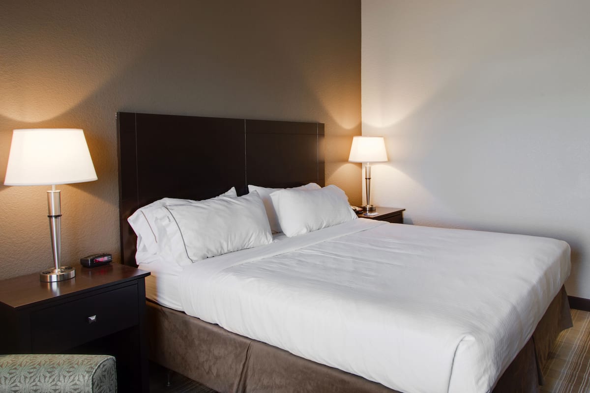 A hotel room with a large bed, two bedside tables with lamps, a small drawer, and a patterned chair.