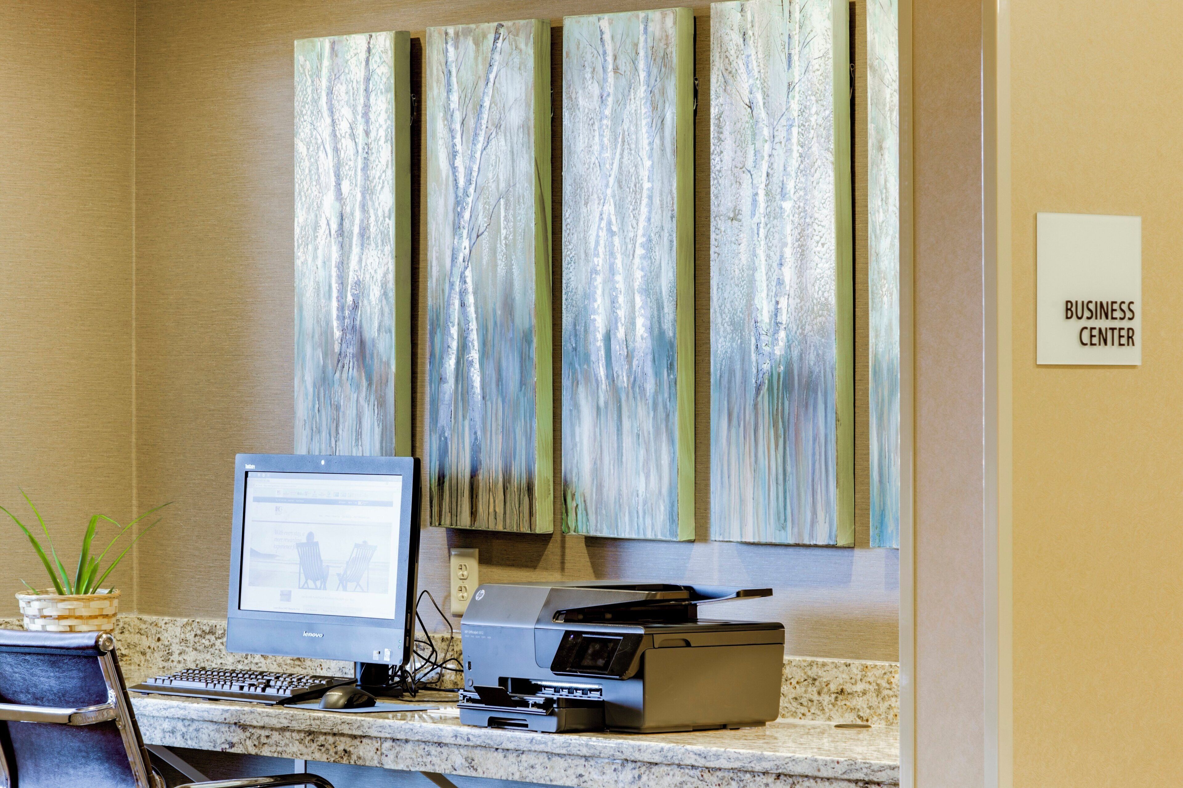 A reception desk with a computer, printer, and a sign indicating the business center.