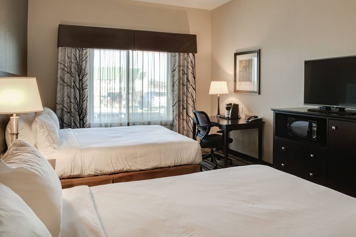 A hotel room with two beds, a desk with a chair, a television, and a window with curtains.