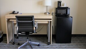 Habitación de hotel con escritorio, silla de oficina negra, lámpara, cafetera y microondas.