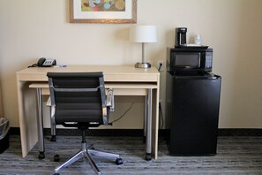 A hotel room with a desk, a black office chair, a lamp, a coffee maker, and a microwave.