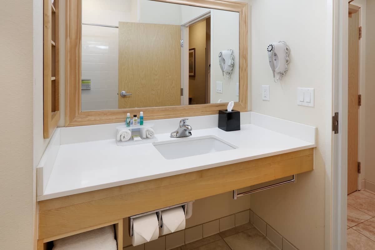 A modern bathroom with a white sink, a large mirror, and a towel rack.