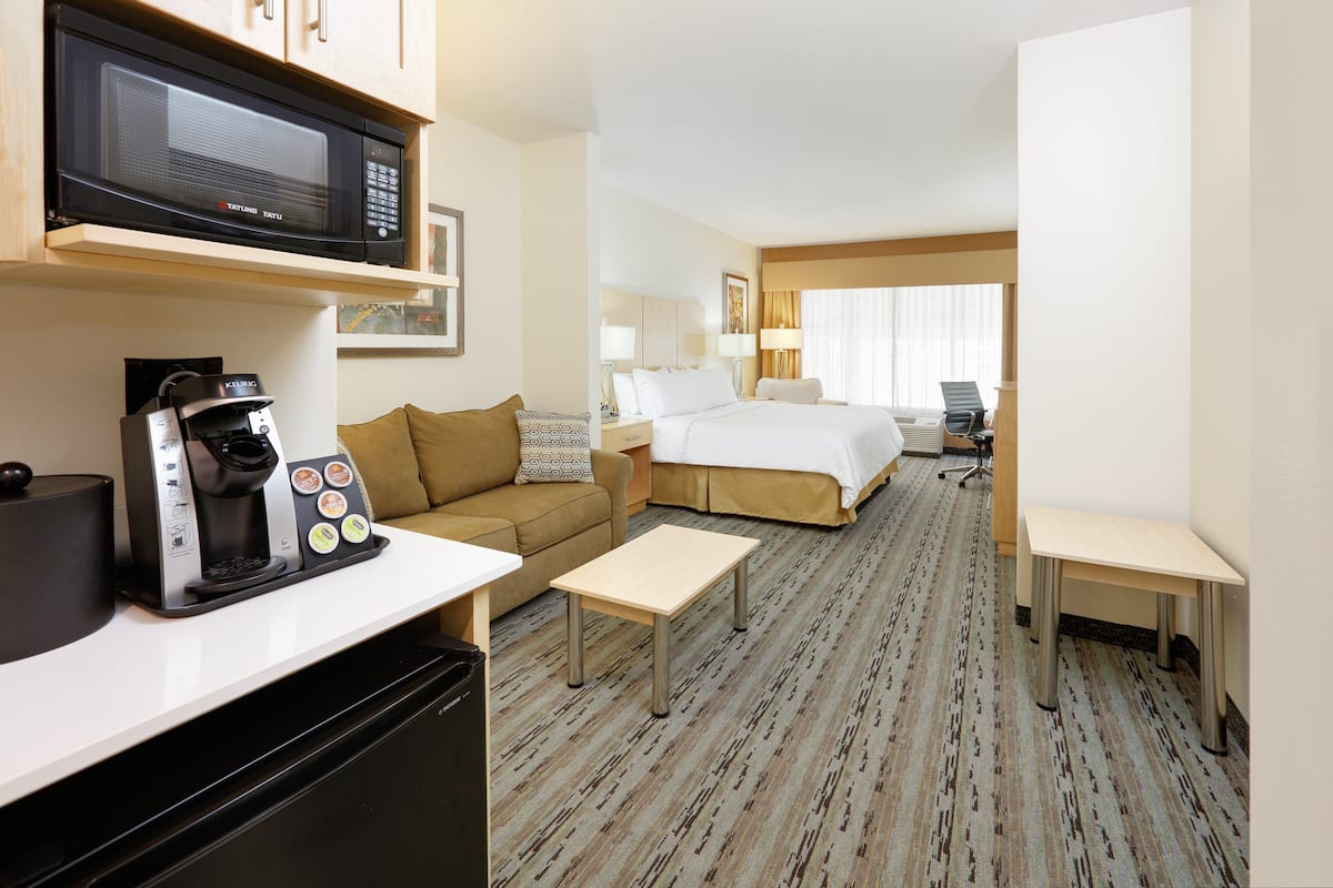 A hotel room with a kitchenette, a bed, a desk, and a chair.