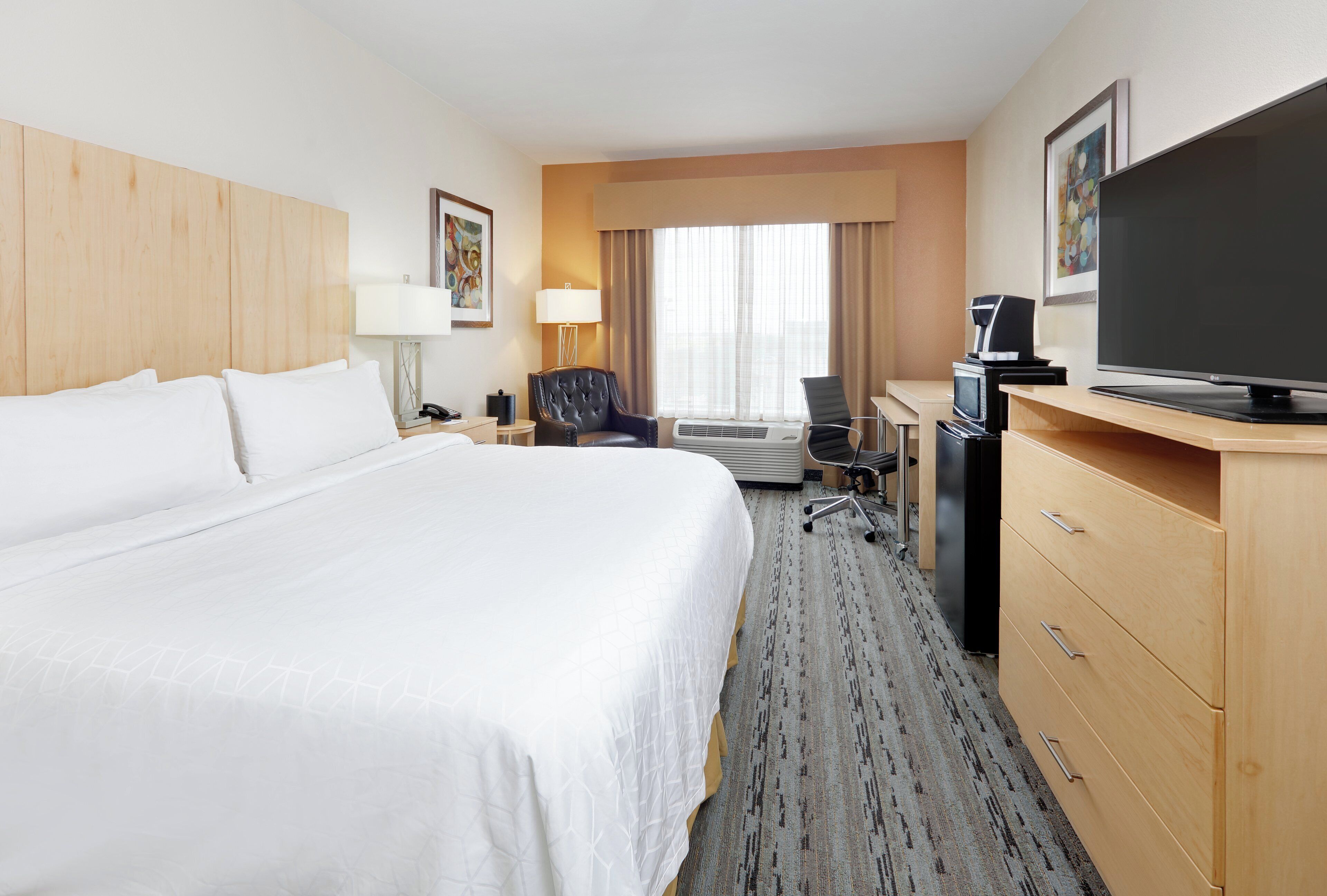 A hotel room with a large bed, a desk with a computer, a television, and a coffee maker.