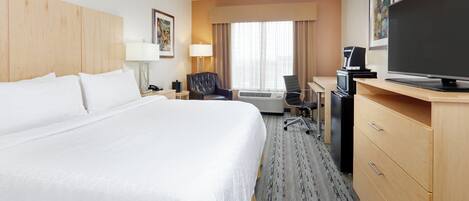 Una habitación de hotel con una cama grande, un escritorio con computadora, un televisor y una cafetera.