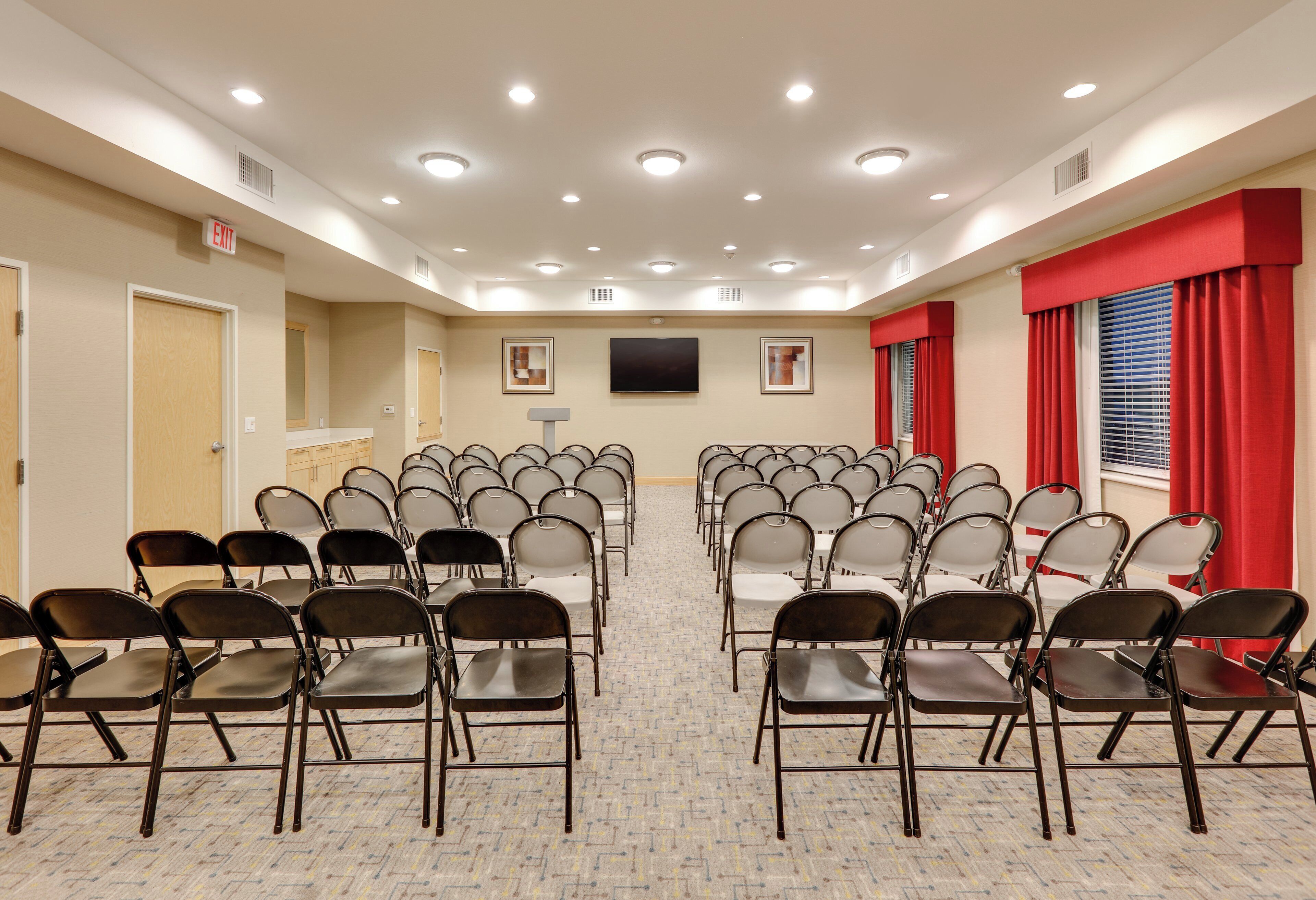 Une salle de conférence avec des rangées de chaises, un téléviseur à écran plat et un sol recouvert de moquette.