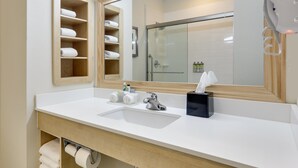 Un baño moderno con un espejo grande, lavamanos blanco y estantes de madera con toallas.