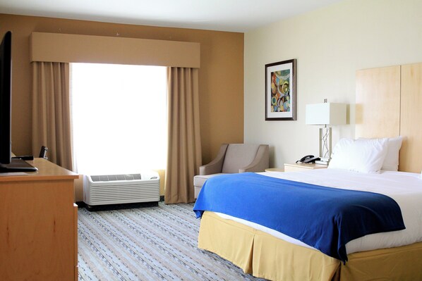 A hotel room with a bed, a desk, a chair, a desk lamp, a telephone, and an air conditioning unit.