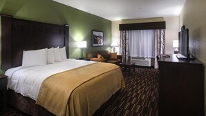 A hotel room with a large bed, a desk, a chair, a TV, and a window with curtains.