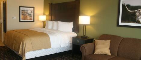 A hotel room with a bed, a brown sofa, a small table, two bedside lamps, and a framed picture on the wall.