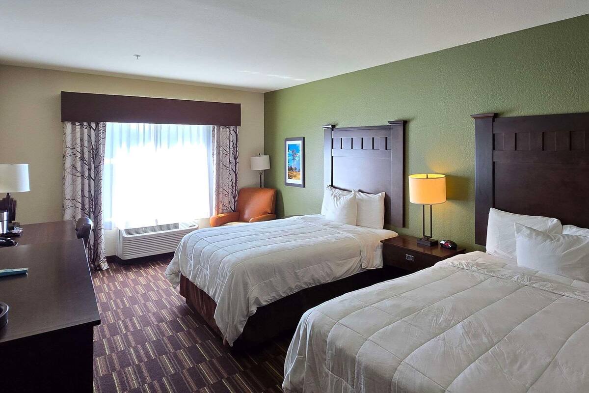 A hotel room with two beds, a desk, a chair, and a window with curtains.