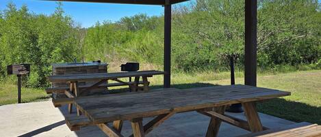 Un área de picnic techada al aire libre con bancos de madera y una parrilla.