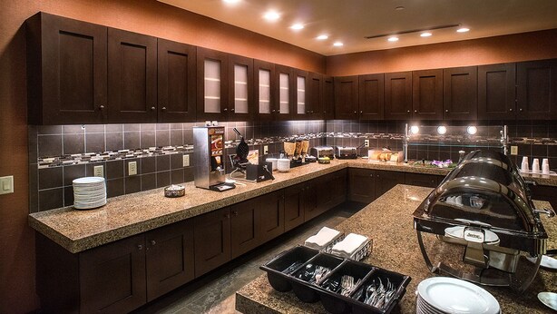A modern kitchen with dark wood cabinets, granite countertops, and a buffet setup with food service equipment.