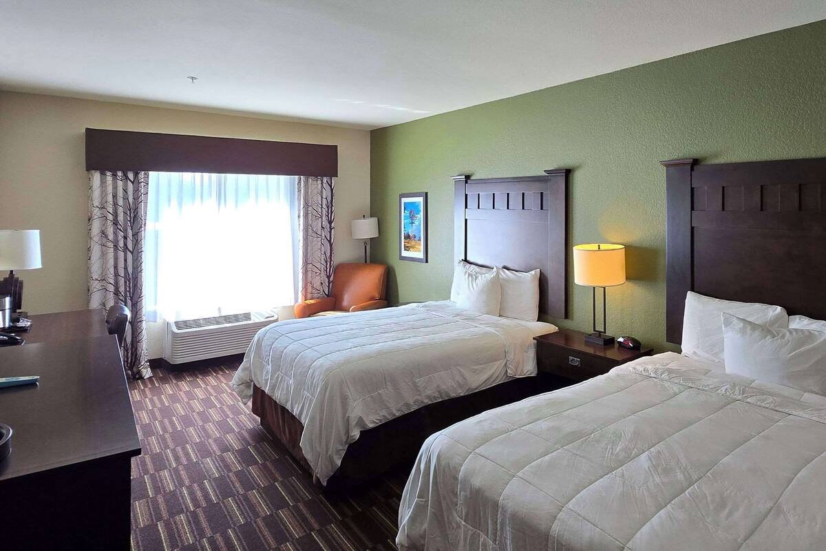 Une chambre d’hôtel avec deux lits, un bureau, une chaise et une fenêtre avec des rideaux.