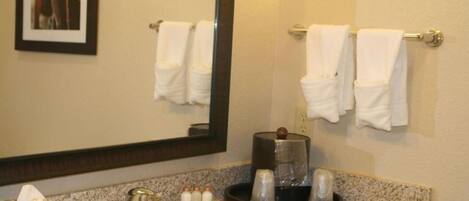 A hotel bathroom with a granite countertop, a sink, a mirror, and two towel racks with white towels.