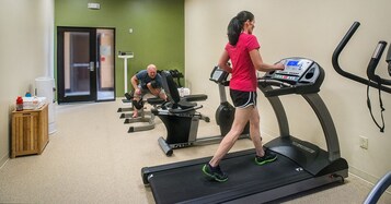 Un gimnasio con cintas de correr, un hombre usando una máquina de pesas y una mujer caminando en una cinta.