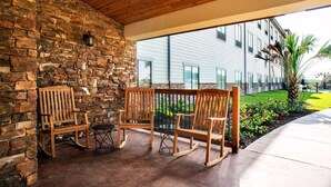 A patio with wooden rocking chairs and a stone wall.