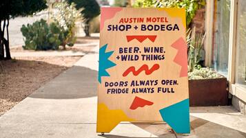 Een houten bordje van Austin Motel Shop + Bodega met daarop een advertentie voor bier, wijn en wild, met de tekst 'deuren altijd open en koelkast altijd vol'.