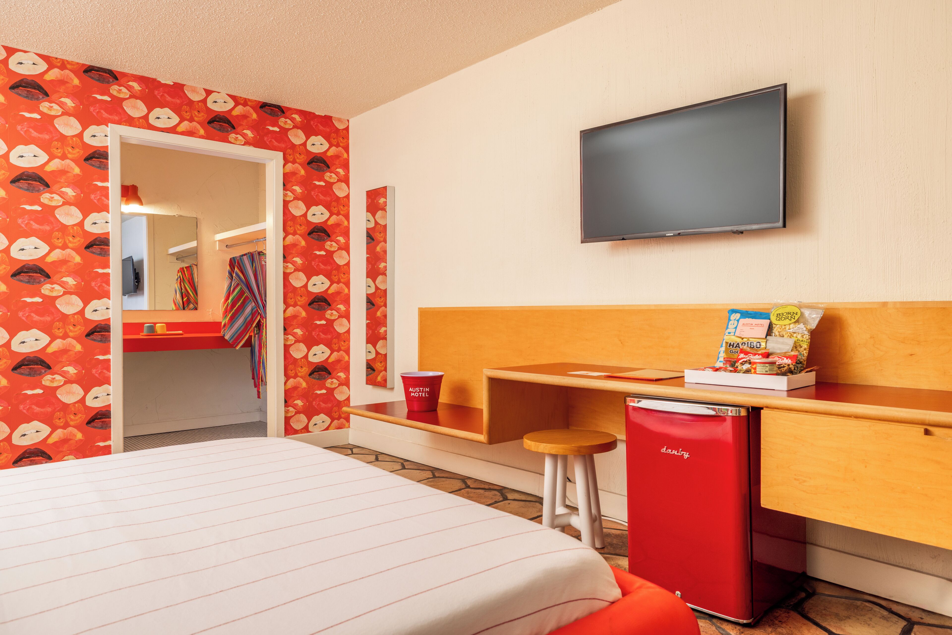 A hotel room with a bed, a desk, a television, and a minibar.