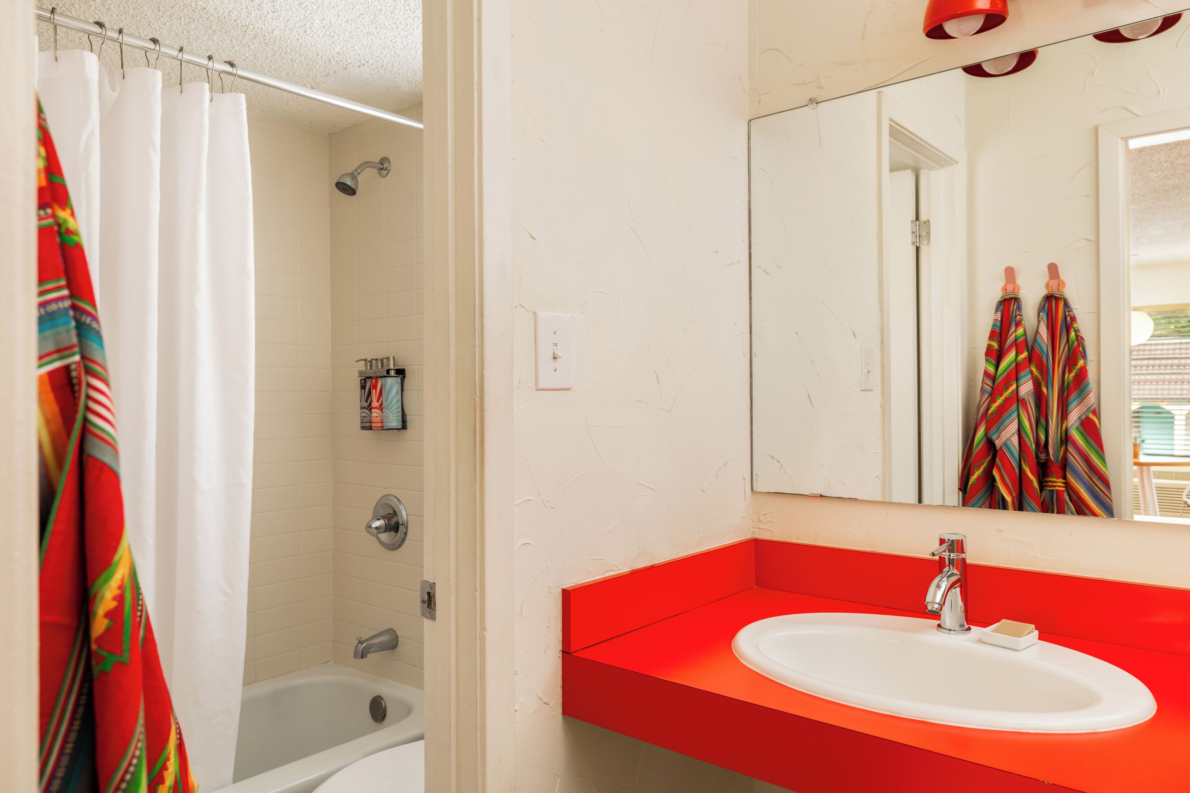 Un baño con una bañera blanca, un lavabo rojo y una cortina de ducha.