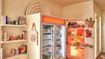 Vestíbulo de hotel con un refrigerador lleno de bebidas, una estantería con libros y una exhibición de aperitivos y artículos pequeños.