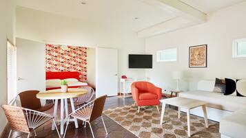 A modern living room with a white sofa, red armchair, and a dining area with wicker chairs.