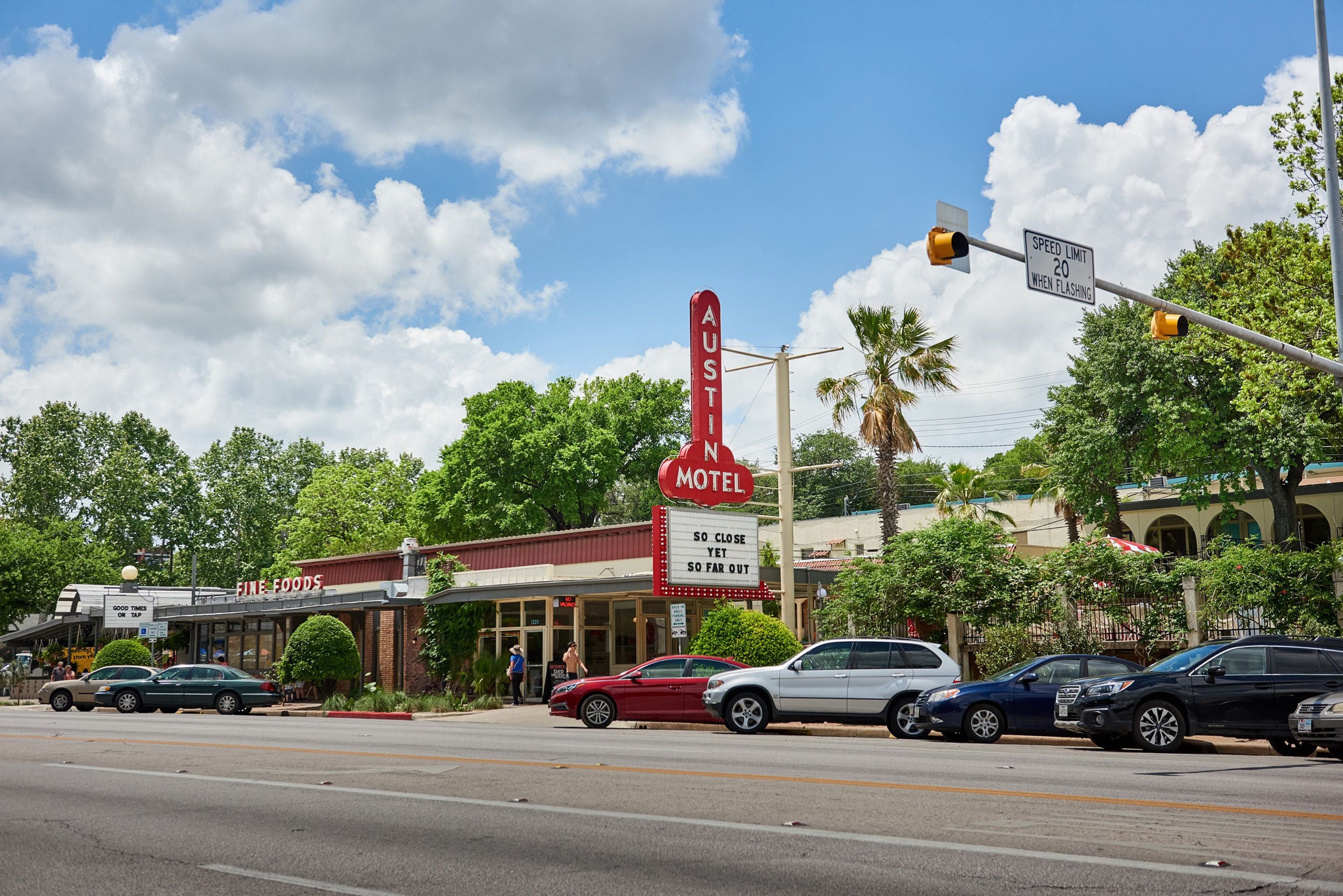 A motel with a neon sign, a speed limit sign, and a traffic light.