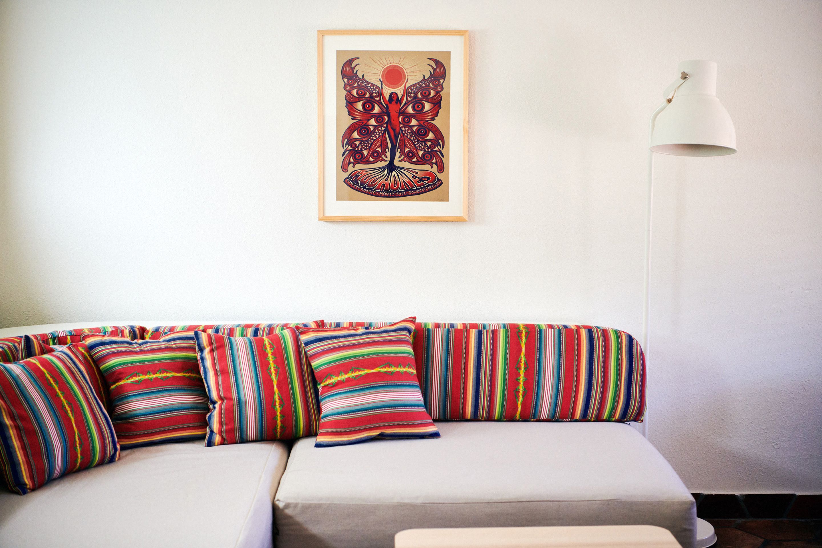 Un salon moderne avec un canapé, des coussins rayés aux couleurs vives, une œuvre d’art encadrée et une lampe sur pied.