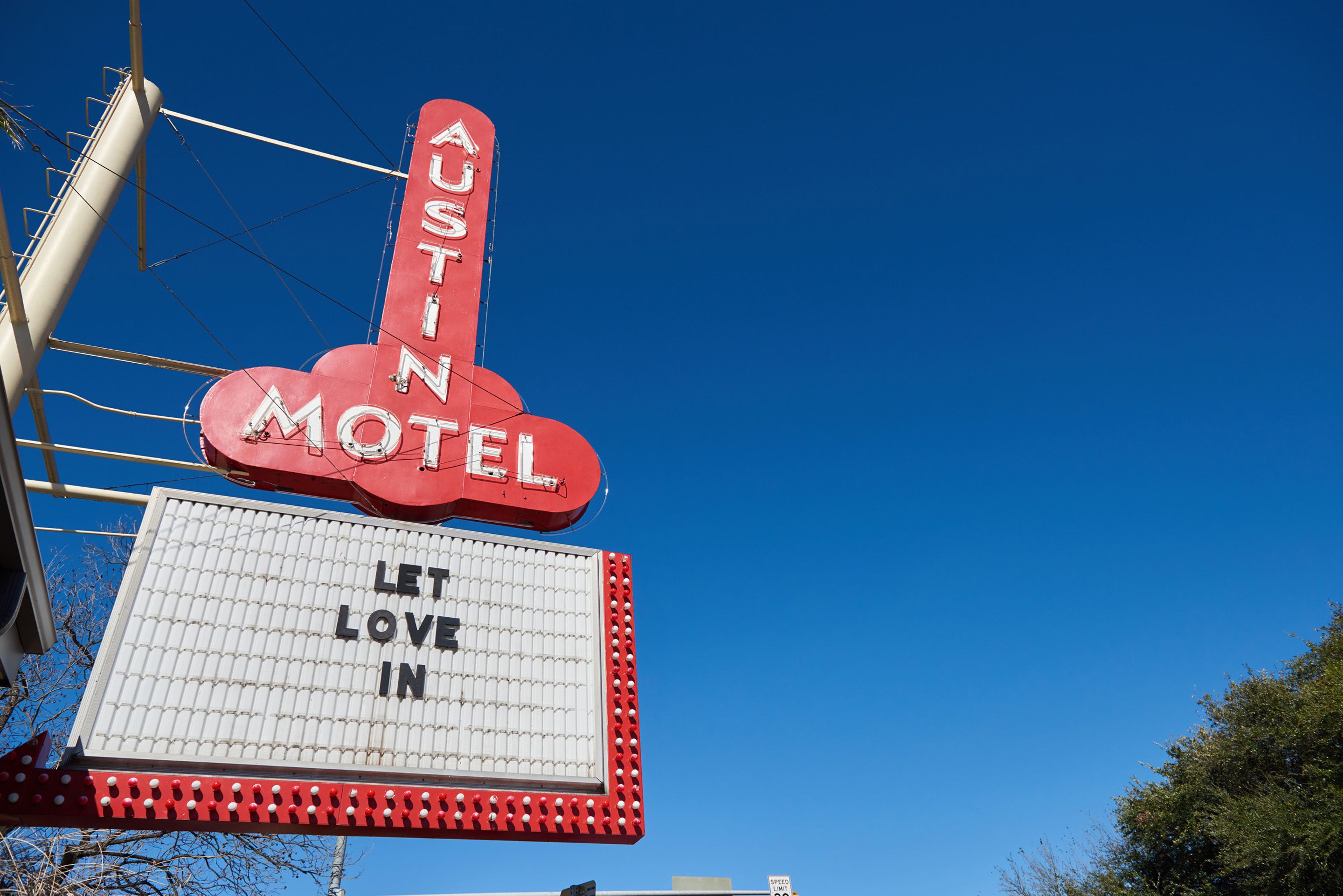 A motel sign with the words "Austin Motel" and "Let Love In" on a clear blue sky background.