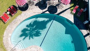 Eine Vogelperspektive auf einen Swimmingpool mit Liegestühlen und Sonnenschirmen, umgeben von einer Steinterrasse.
