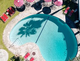 An aerial view of a swimming pool with lounge chairs and umbrellas, surrounded by a stone deck.