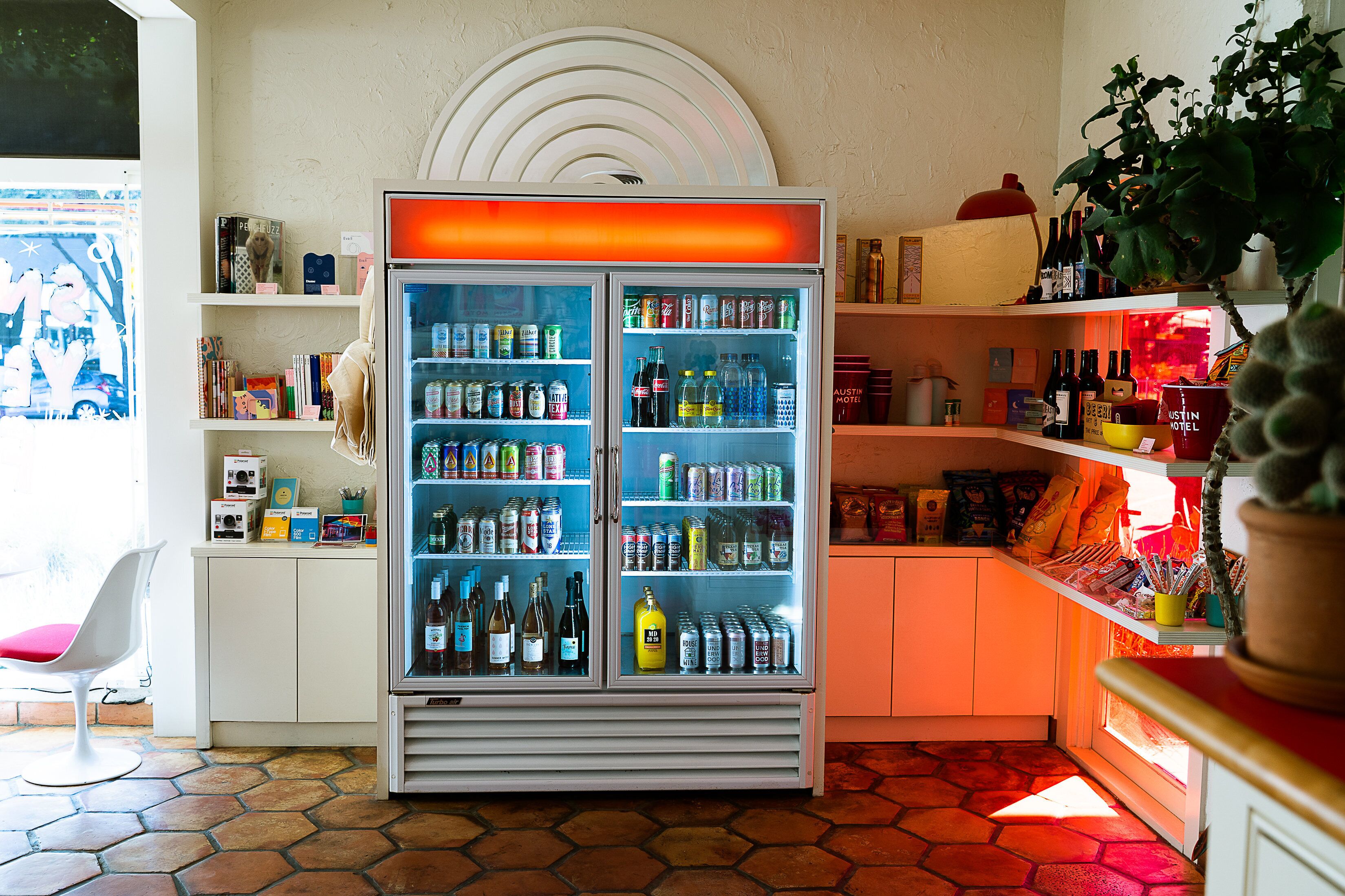 A hotel room with a minibar, a refrigerator stocked with beverages, a window with a view, and a potted plant.