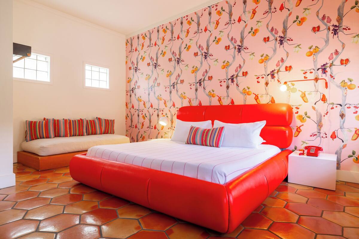 A bedroom with a red bed, a sofa bed, and a patterned wall.