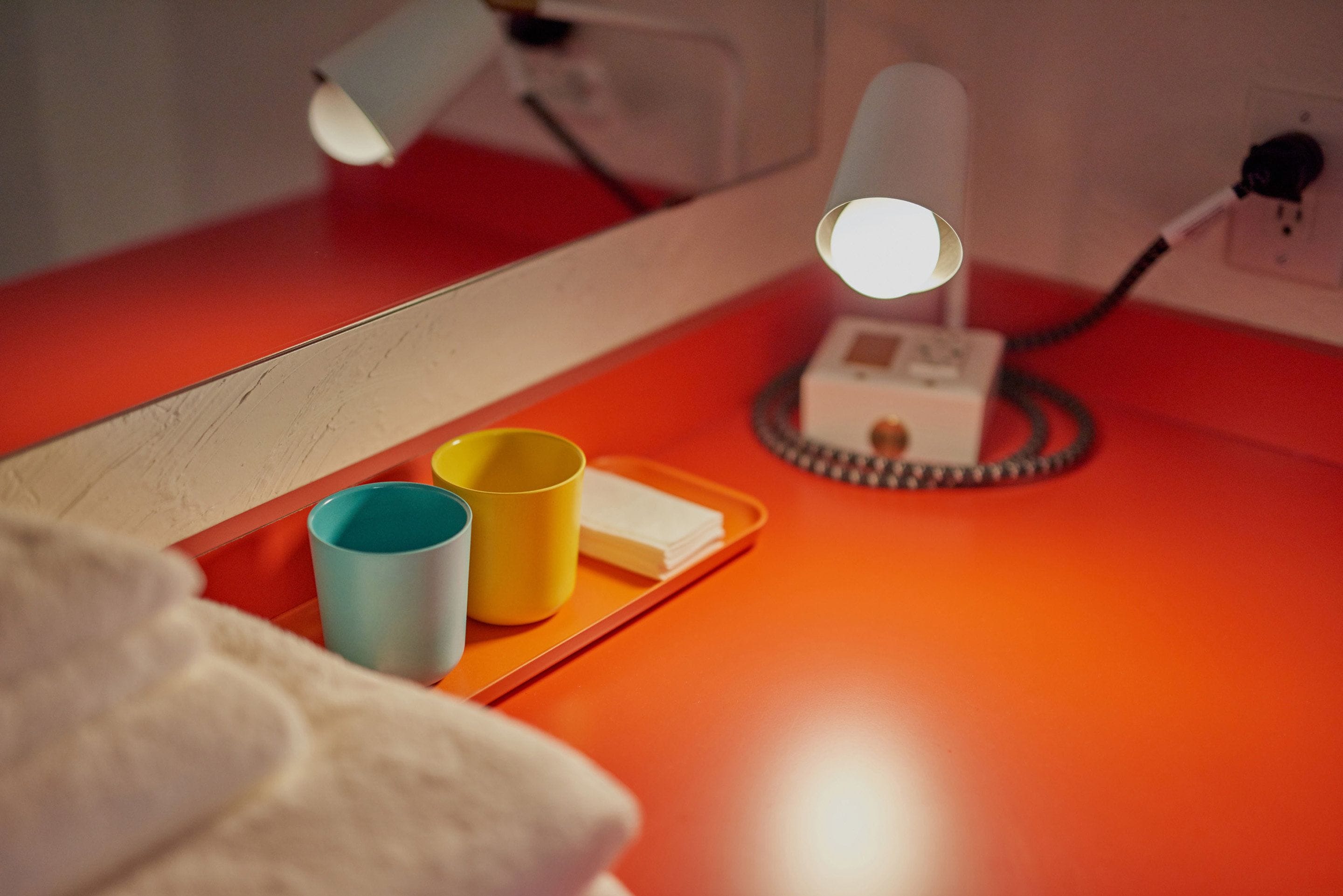 A red bedside table with a lamp, two cups, and a tissue box.