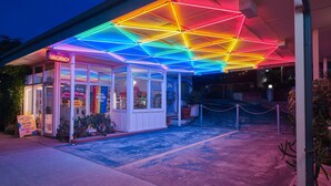 Ein Motel mit einer neonbeleuchteten, geometrischen Decke, einem 'VACANCY'-Schild und einem Banner mit der Aufschrift 'YALL MEANS ALL!'