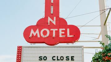 Een motelteken met 'AUSTIN MOTEL' en de tekst 'ZO DICHTBIJ, ZOVER Weg'.