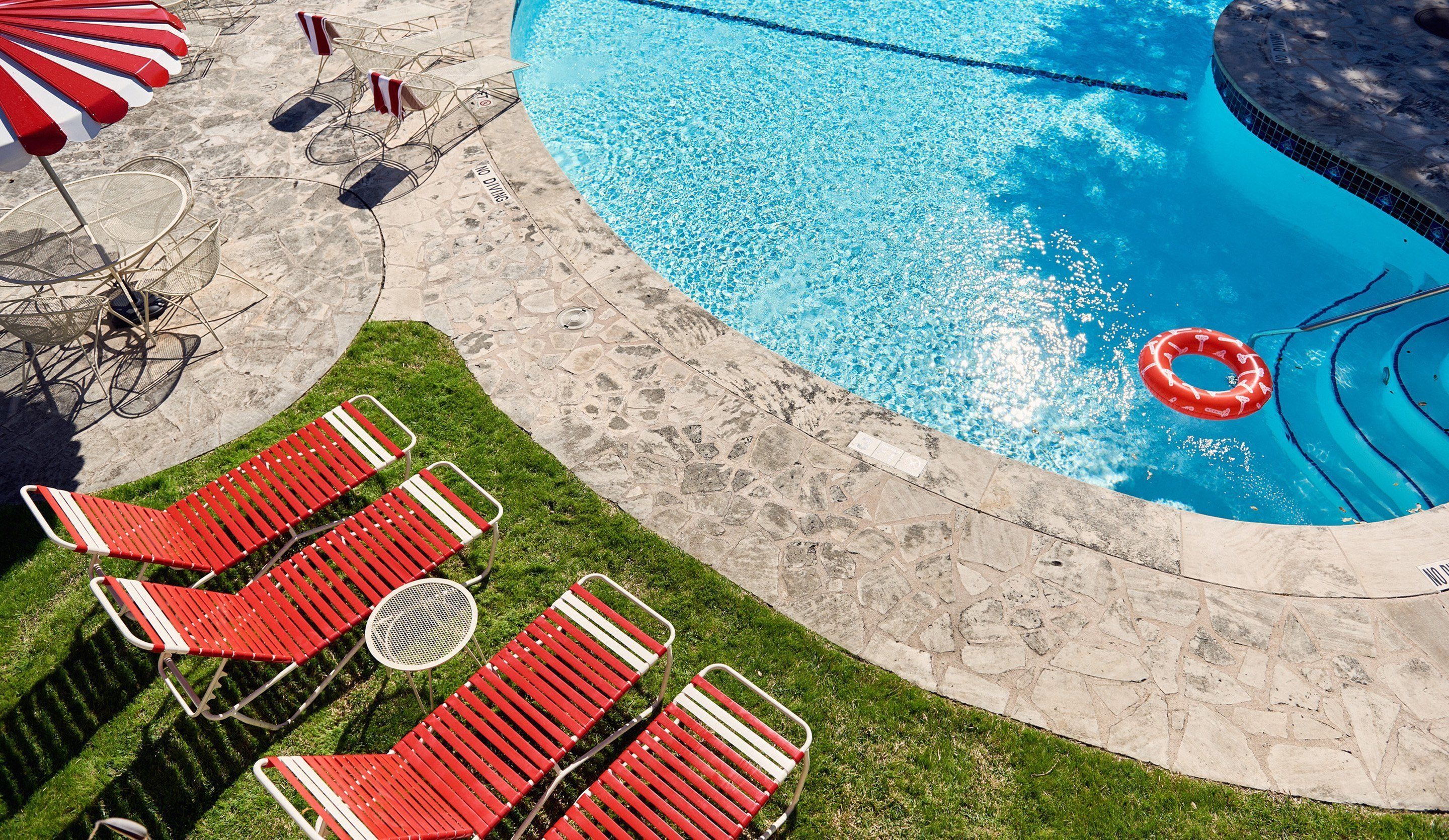 Una piscina con plataforma de piedra, sillas de descanso rojas y blancas, y un letrero de prohibido bucear.